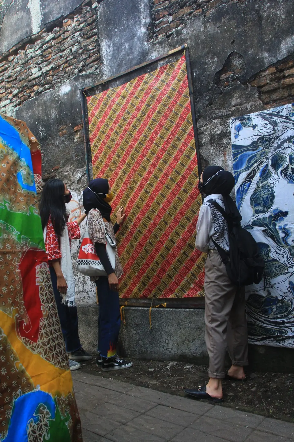 Pengunjung berfoto di gang dengan mural dan kain batik di dinding